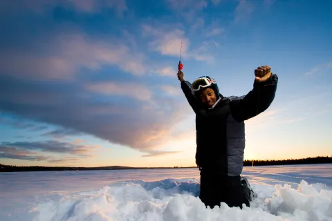 En person i vinterkläder på isen som håller ett fiskespö