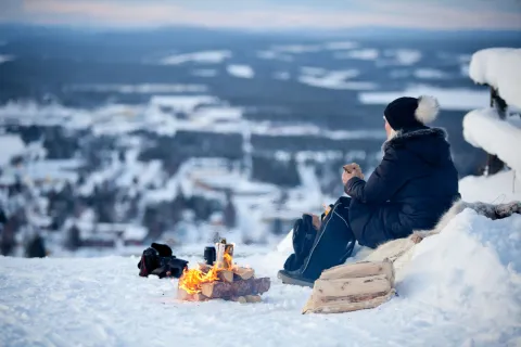 En person som sitter på en snötäckt kulle med en eld
